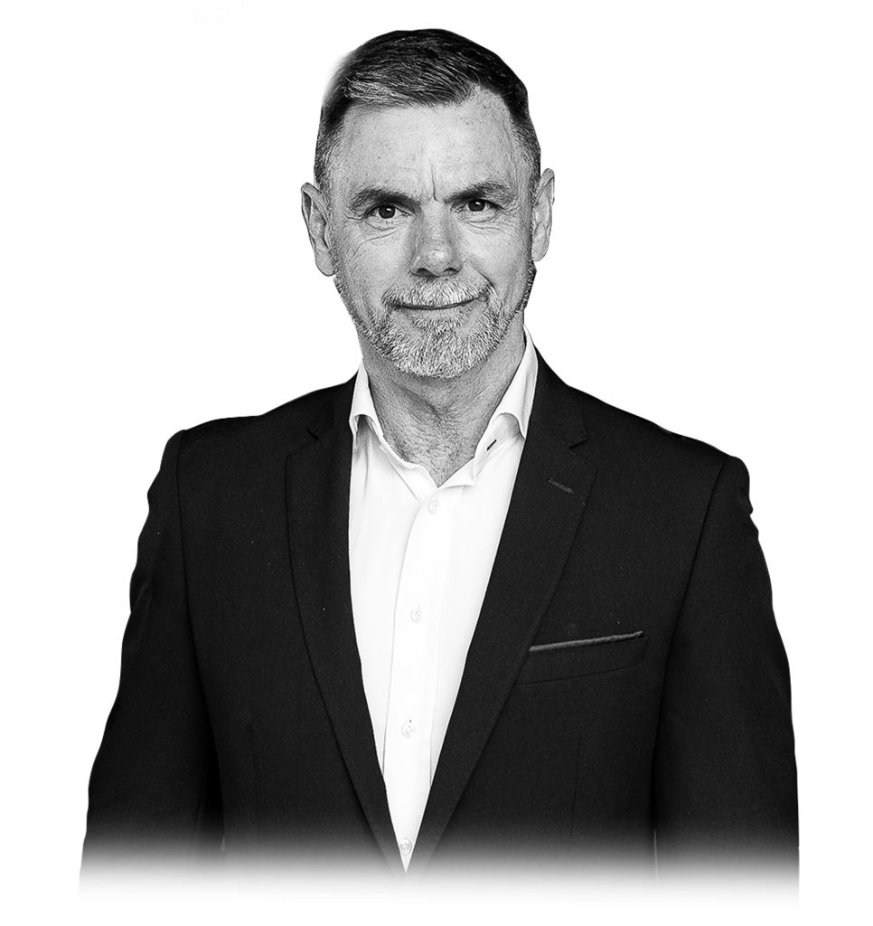 Smartly dressed man in a suit, smiling confidently. Black and white portrait with a plain background.