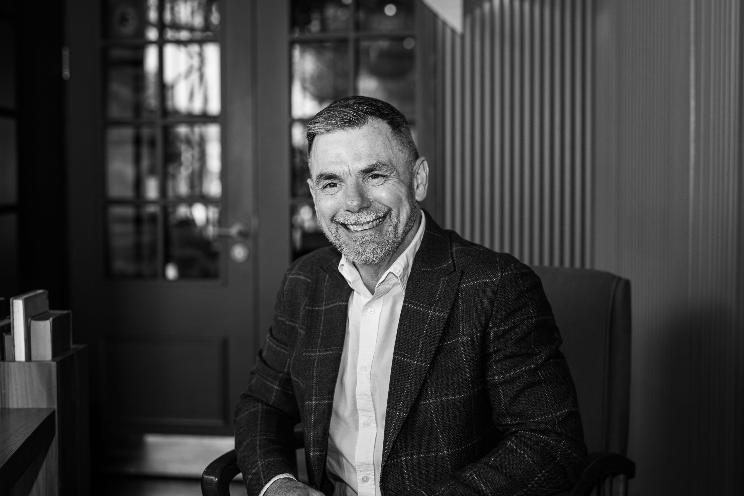 Gary smiling in suit sitting indoors, black and white portrait.